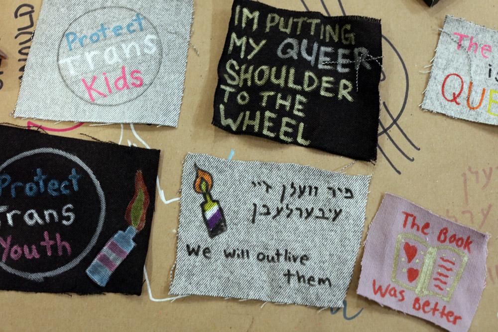 image of cloth patches on a table that have pro-trans messages, including 'Protect Trans Kids | Protect Trans Youth | I'm Putting my Queer Shoulder to the Wheel'