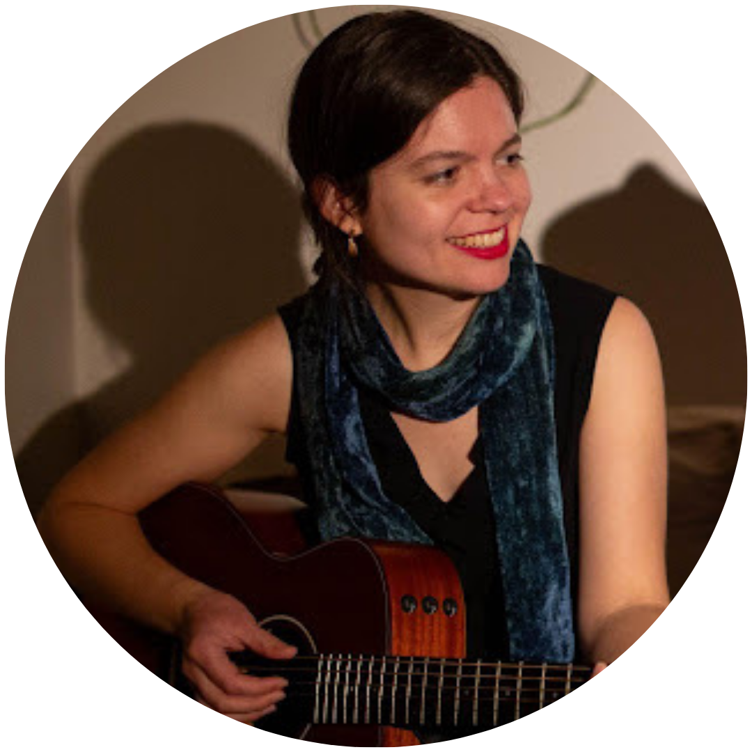 image of a woman with brown hair in a ponytail playing a guitar and smiling during a performance