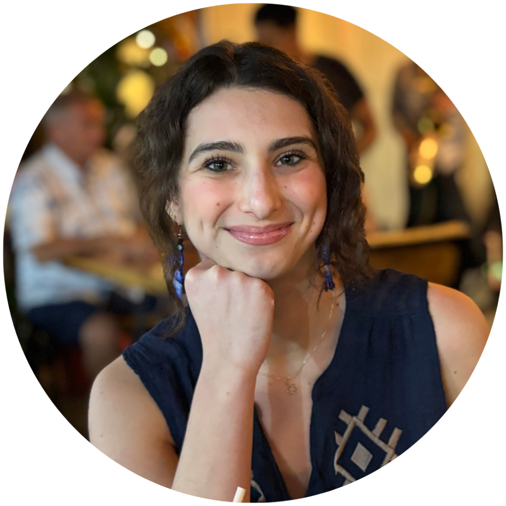 headshot of Lilian Kleinberg, a white woman with dark brown hair - she is smiling at the camera with her head resting on her fist