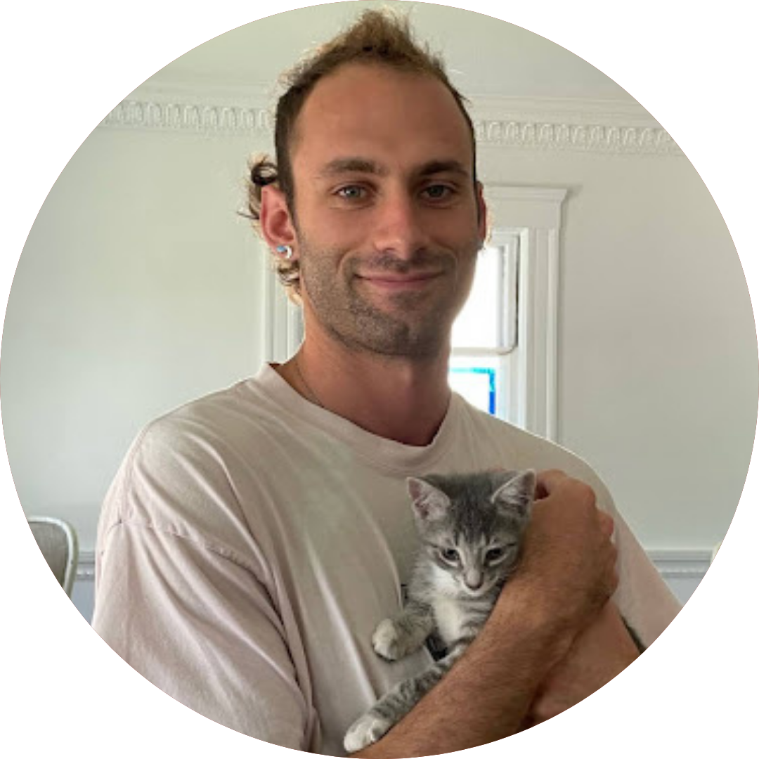 headshot of Ari, a person with brown hair and facial hair holding a kitten