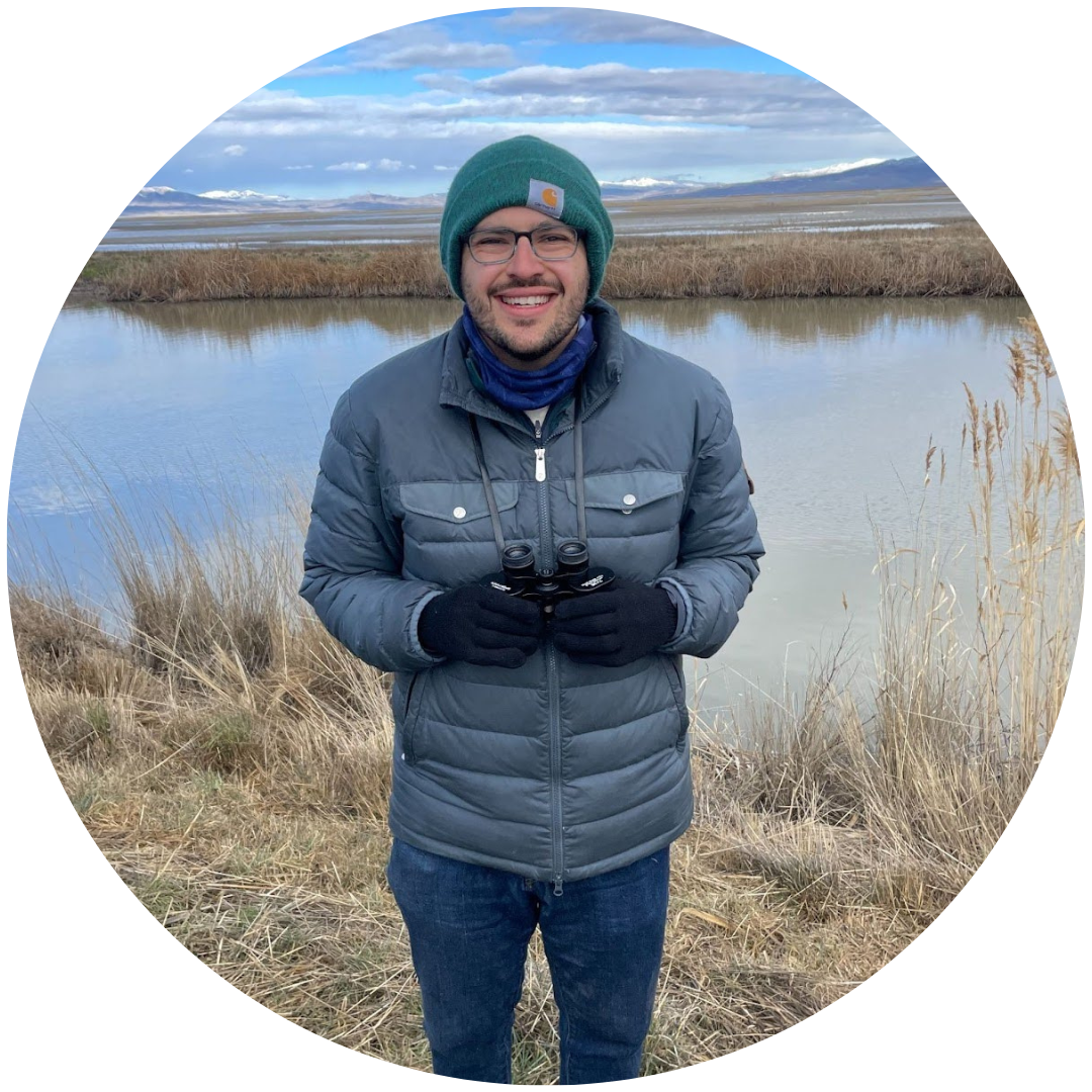 a man in a green hat and blue coat holding binoculars and smiling for the camera outside